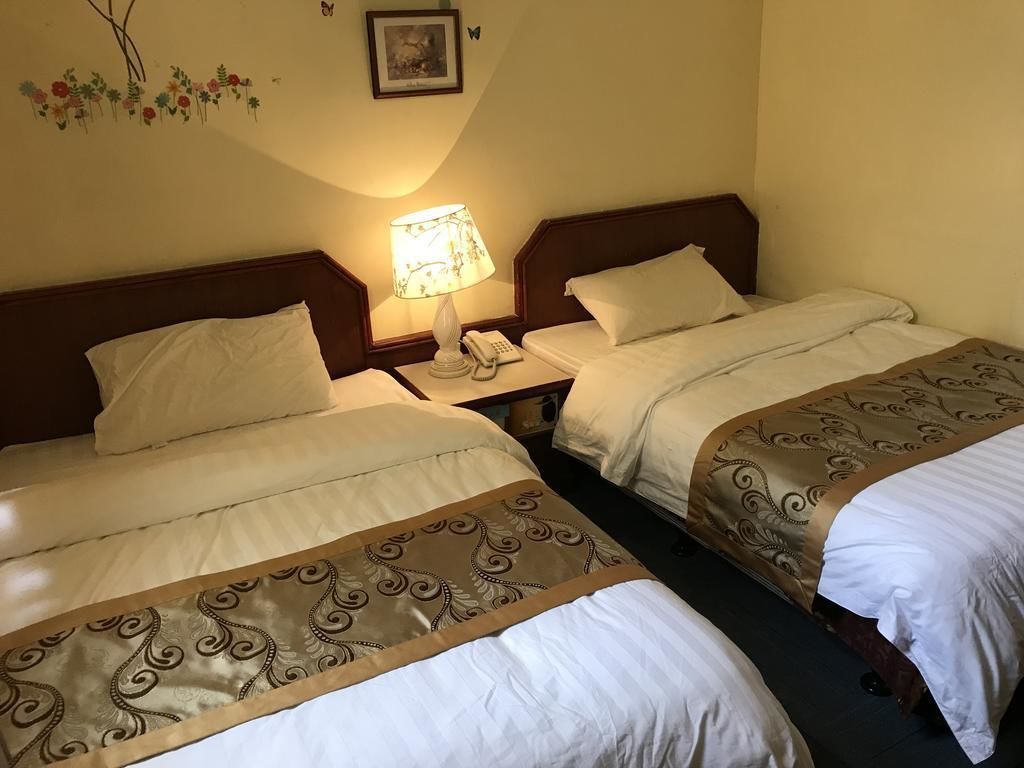 A hotel room with two beds, each with a headboard, a bedside table with a lamp, and a telephone.
