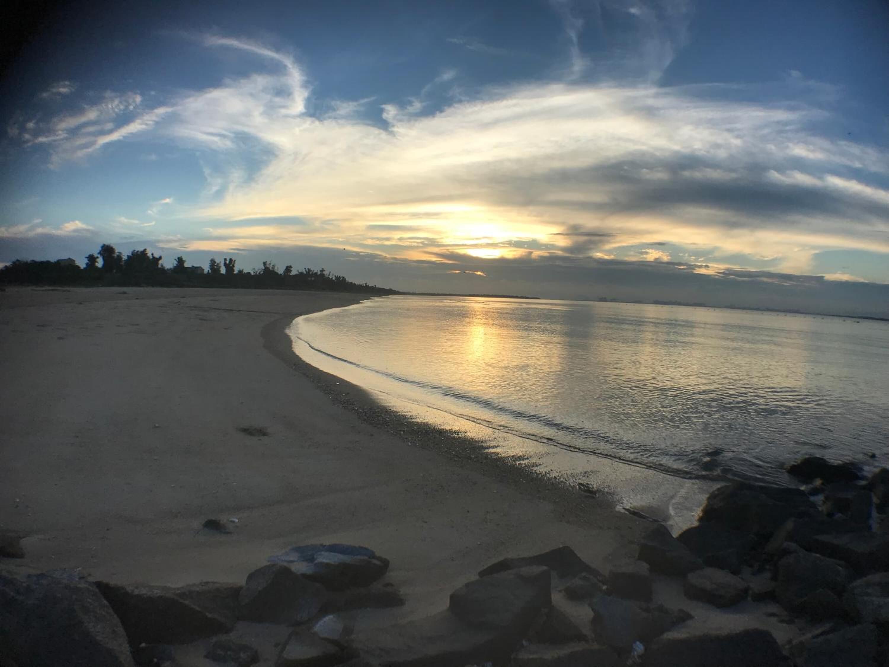 A beach with a curved shoreline, calm water, and a sunset in the background.