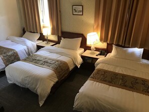 Three single beds with white comforters and decorative headboards, a nightstand with a lamp and telephone, and a framed picture adorn this inviting room.