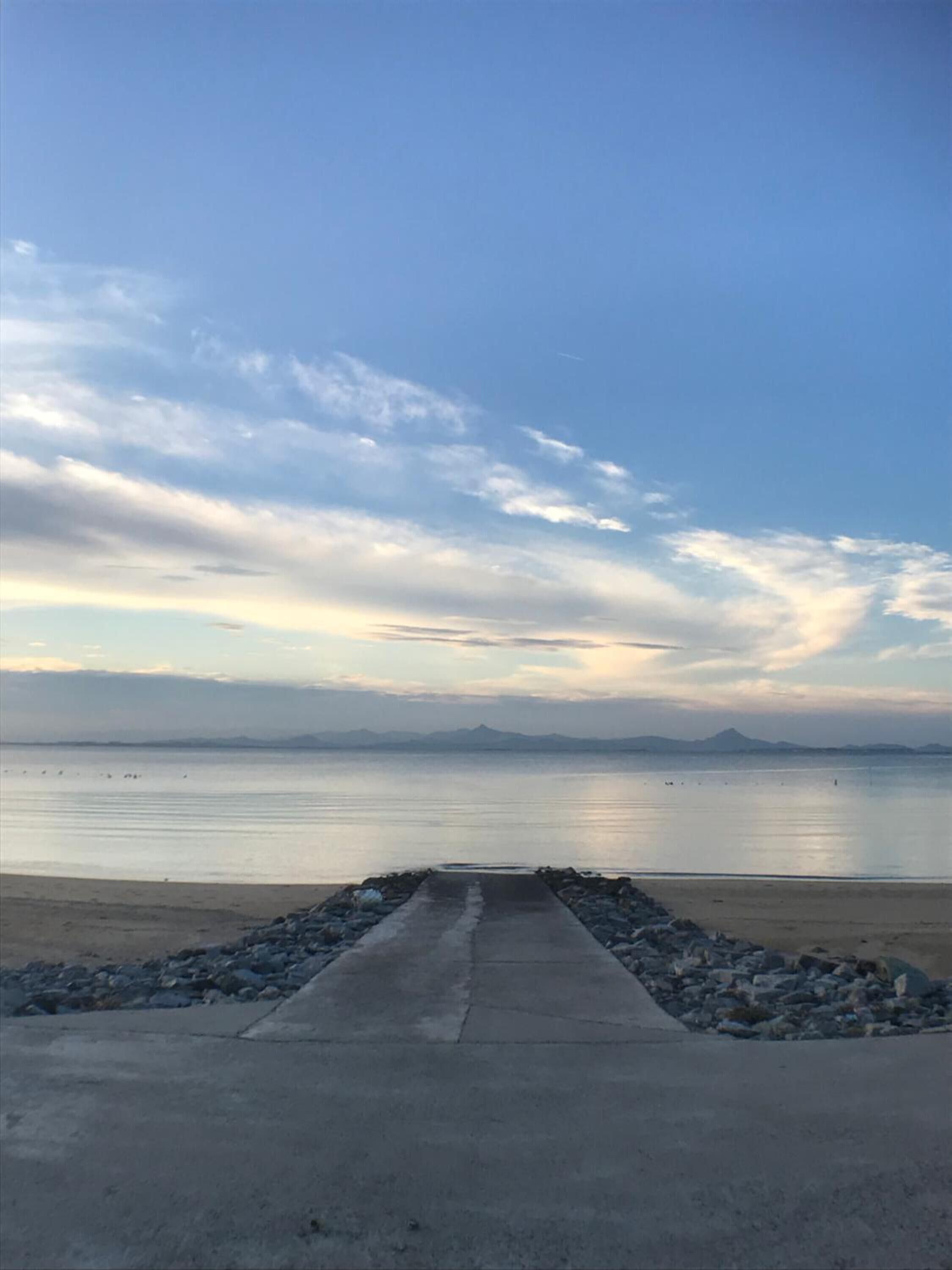 A concrete pathway leading to a calm body of water with distant mountains.