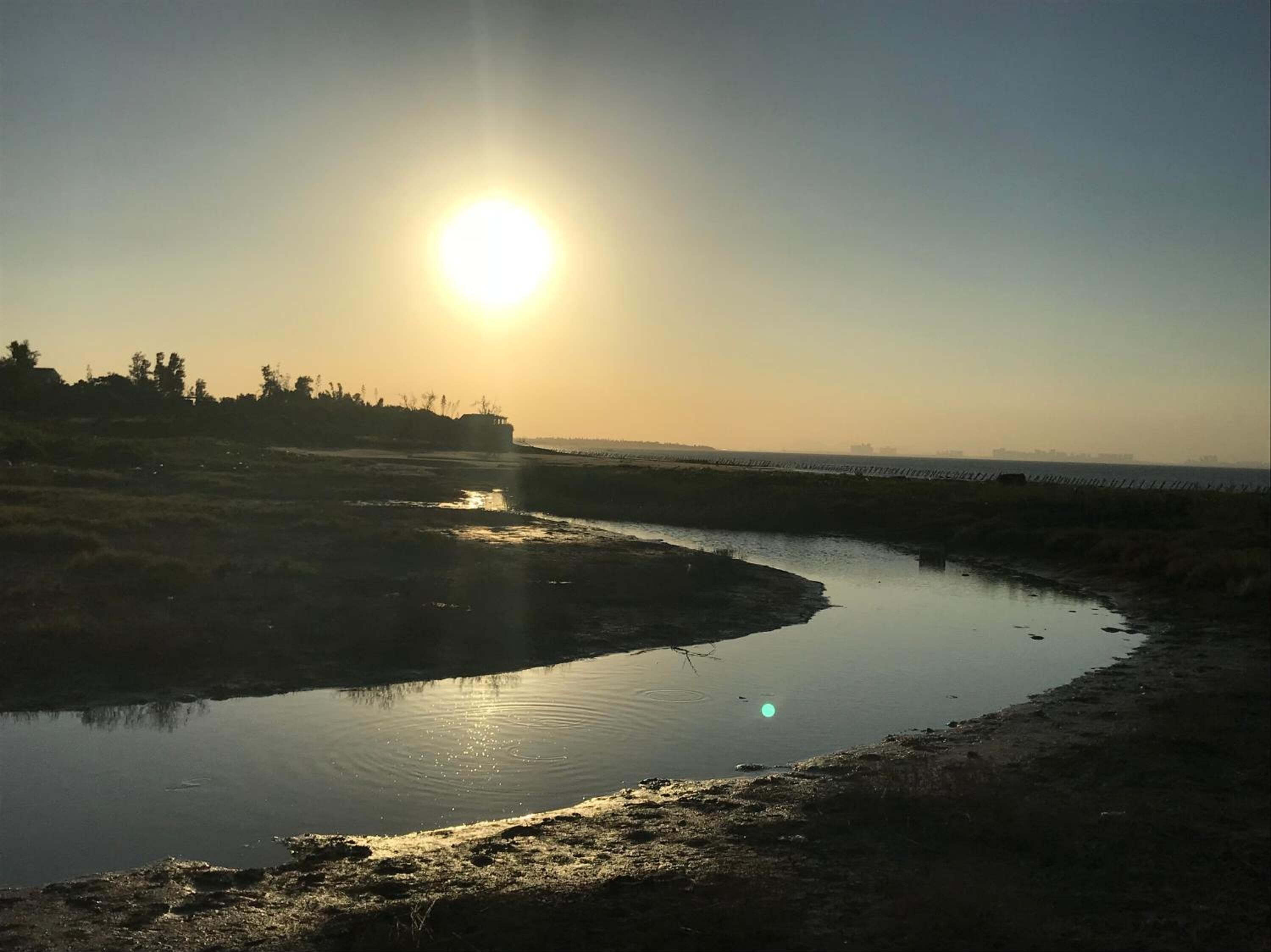 A river at sunrise with the sun low on the horizon, reflecting on the water.