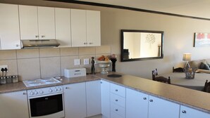 A modern kitchen with white cabinets, a built-in oven, and a countertop with a bread box. - Santini Village 103 (Plettenberg Bay)