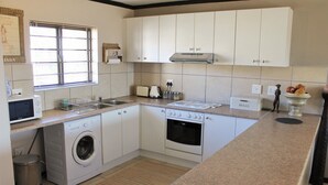 A compact kitchen with a washing machine, a microwave, a toaster, and a bread maker. - Santini Village 103 (Plettenberg Bay)