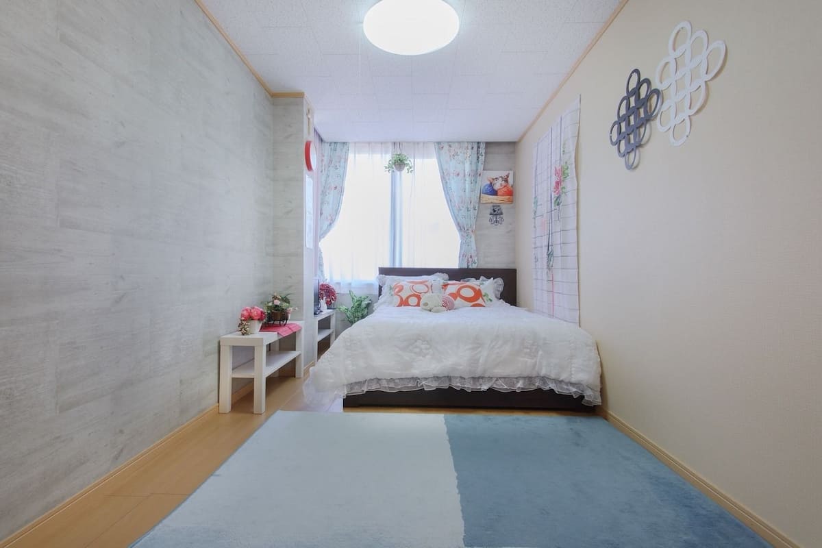 A bedroom with a bed, a small table, a window with curtains, and a wall decoration.