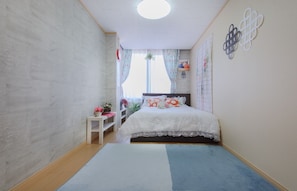 Ein Schlafzimmer mit einem Bett, einem kleinen Tisch, einem Fenster mit Vorhängen und einer Wanddekoration.