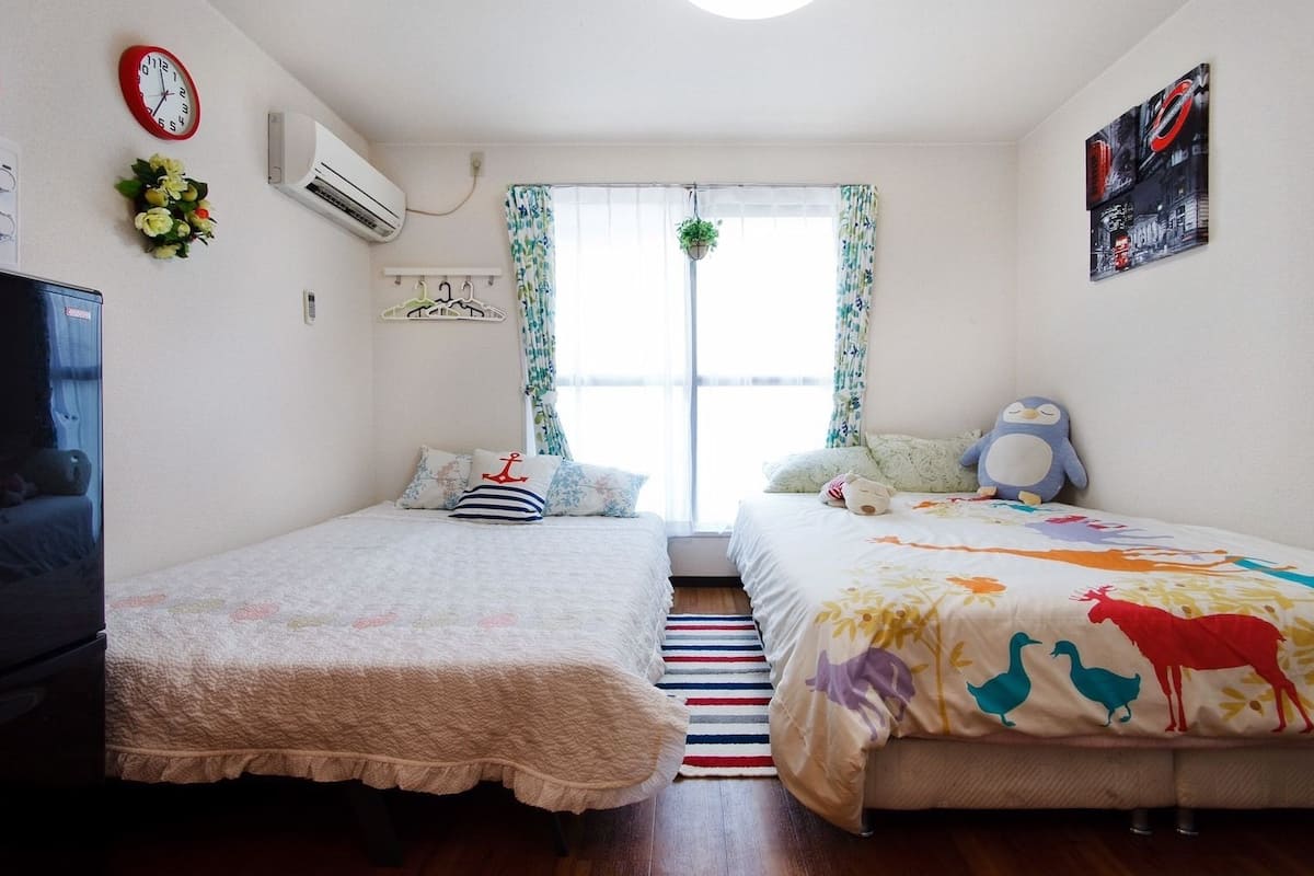 A bedroom with two beds, a TV, a clock, and a window with curtains.