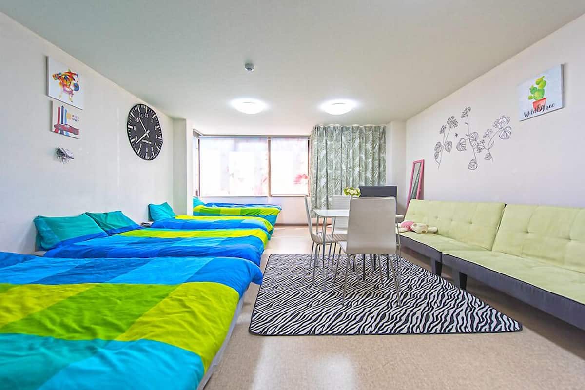 A hotel room with multiple beds, a zebra-patterned rug, a desk, and a green sofa.