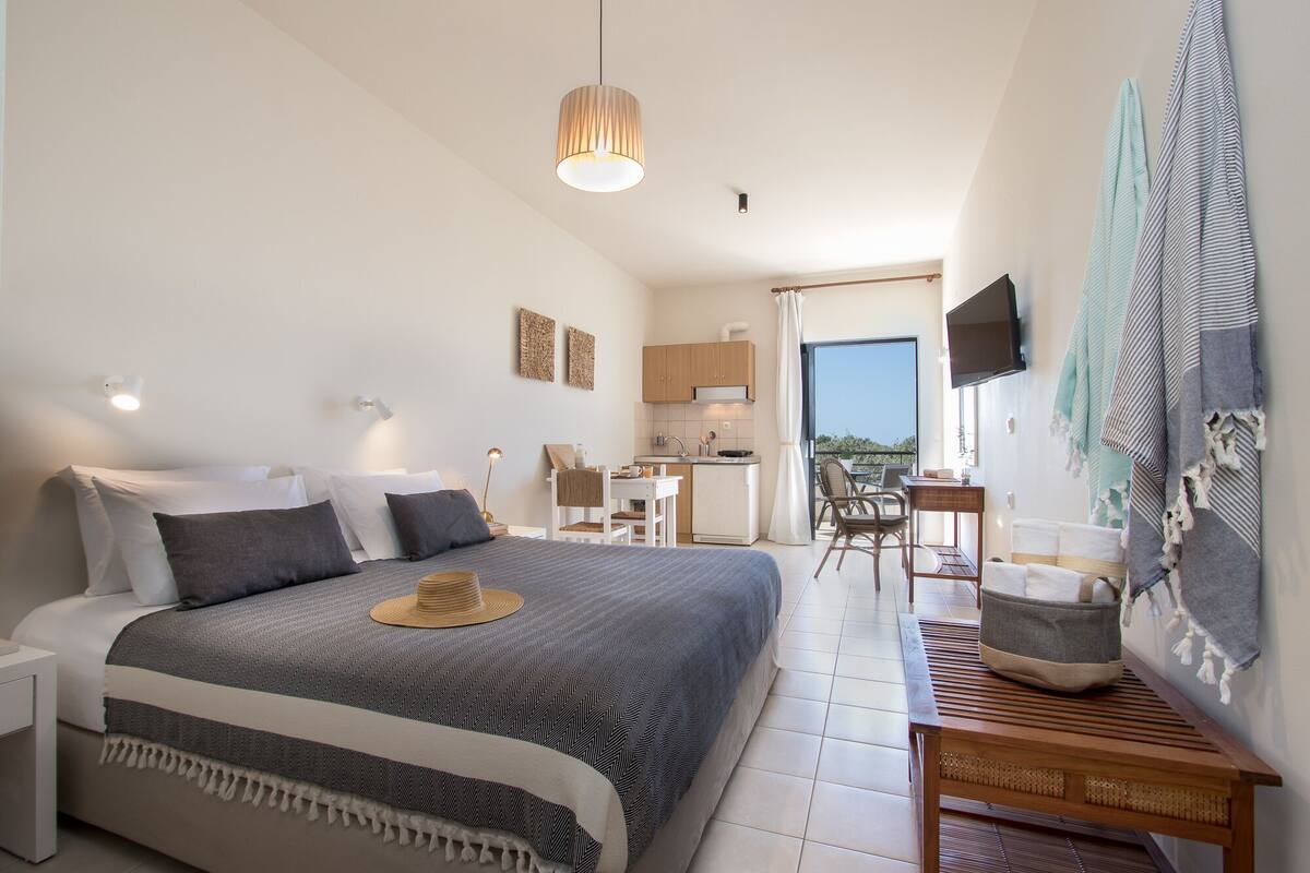 A modern bedroom with a large bed, bedside tables, a desk, and a view of the outdoors.