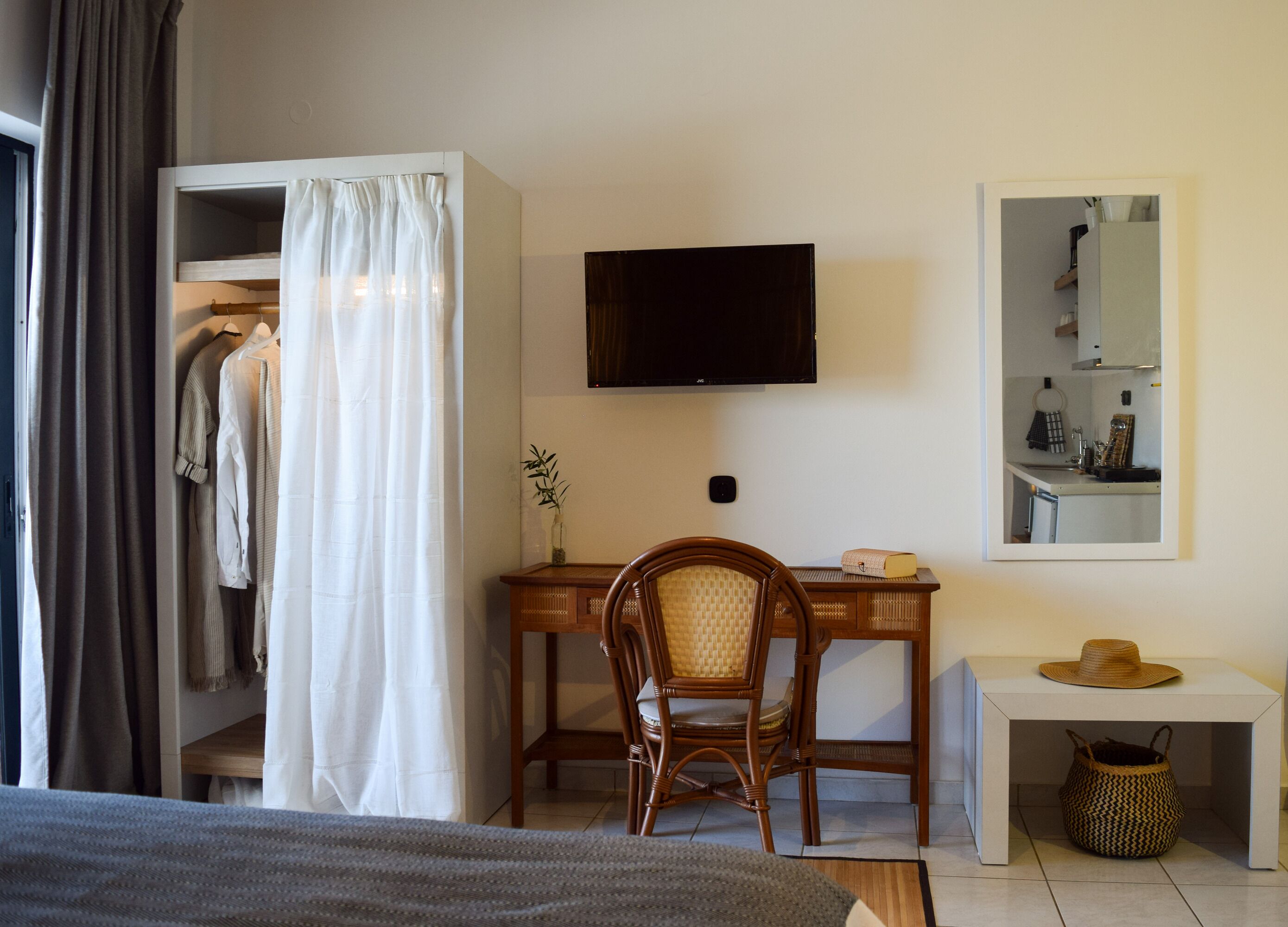A bedroom with a bed, a desk with a chair, a TV, a mirror, and a wardrobe.