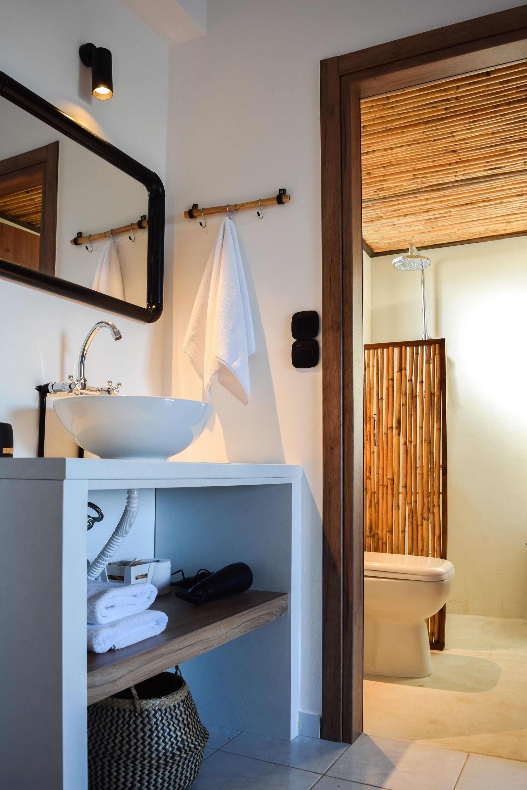 Un baño moderno con un lavabo blanco, un espejo y un cerramiento de ducha de bambú.