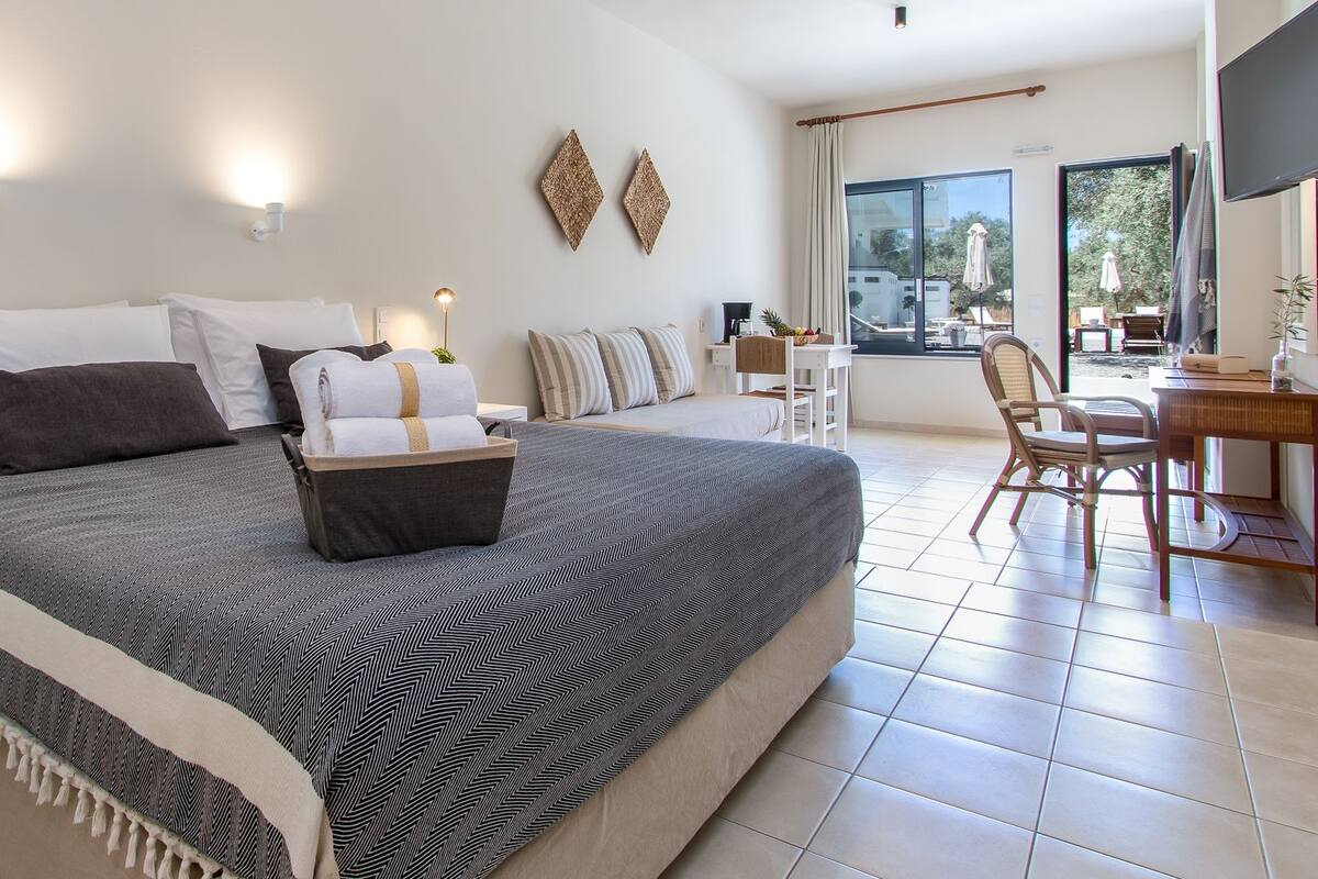 A modern hotel room with a large bed, a desk, and a view of the outdoors.
