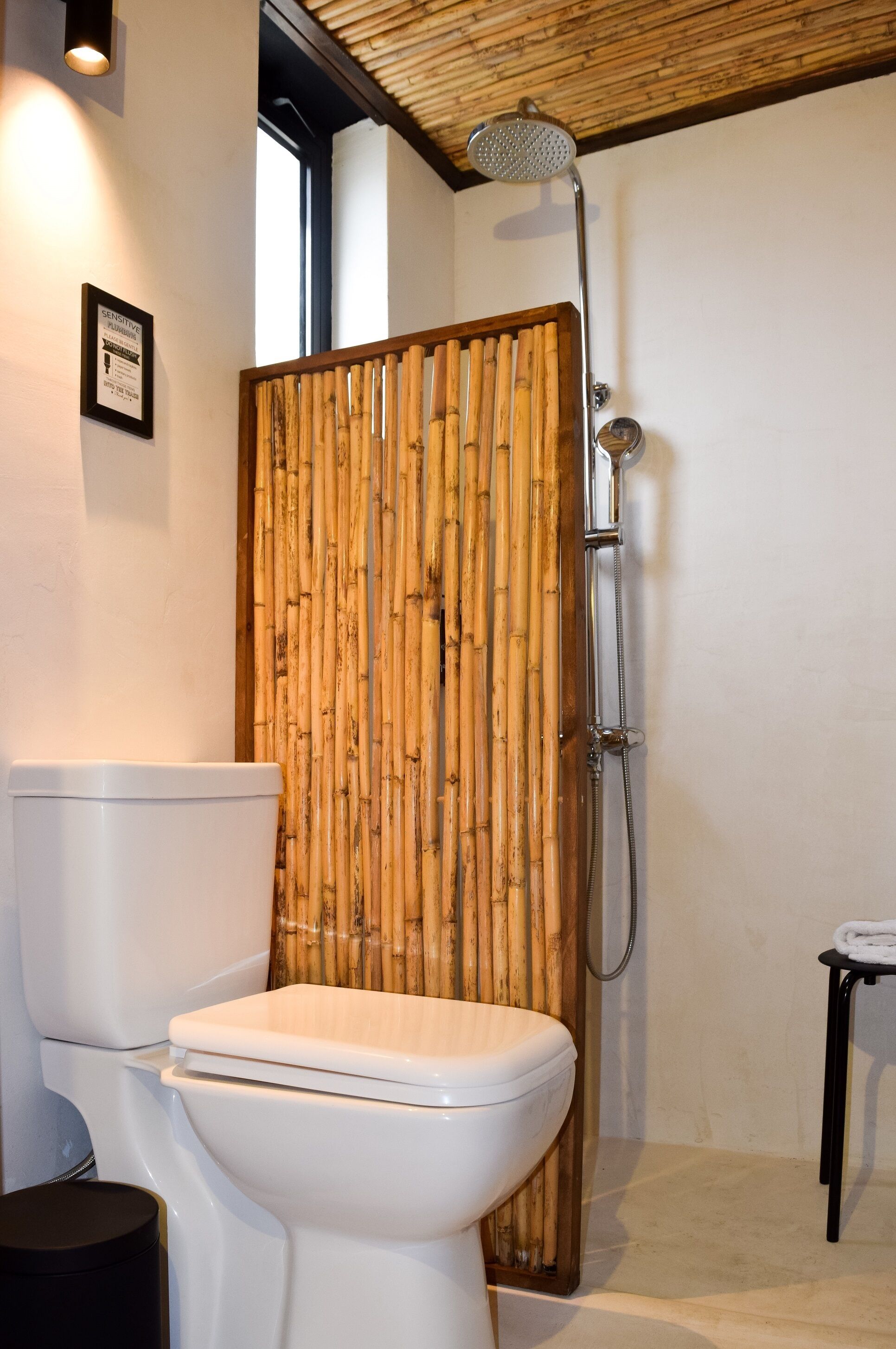 A bathroom with a bamboo shower enclosure, a white toilet, and a small black trash bin.