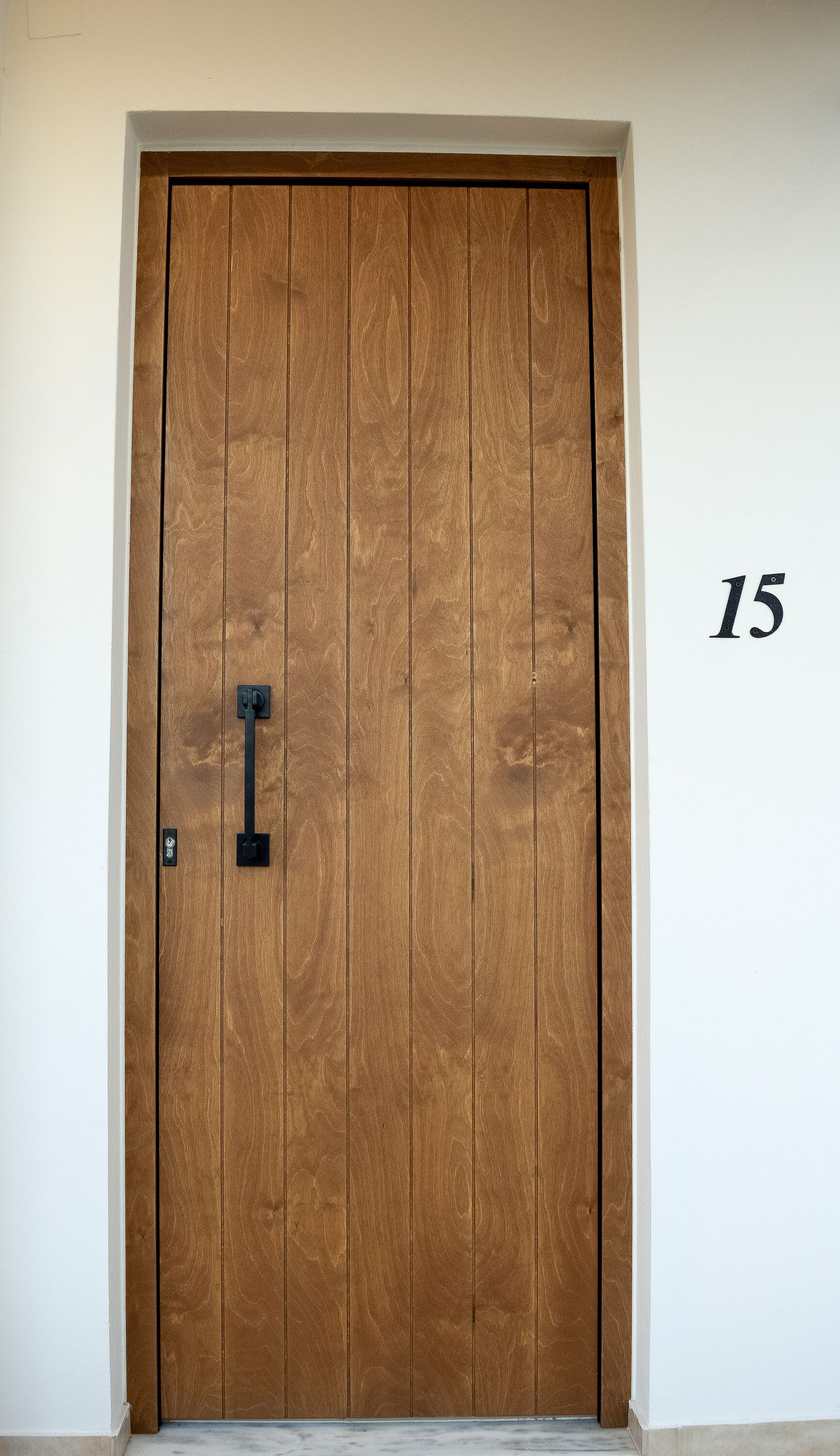 A wooden door with a black handle and a number "15" on the wall beside it.