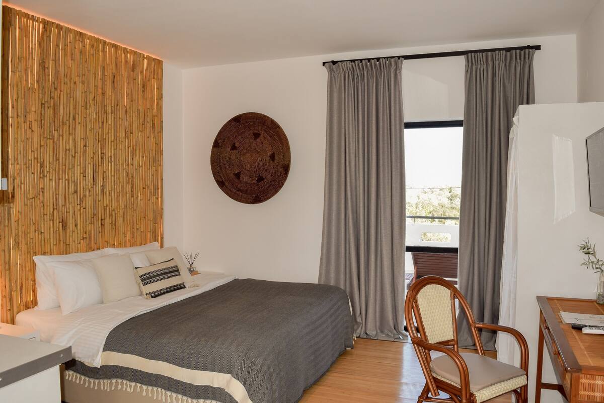A modern bedroom with a large bed, a wooden headboard, a round wall decoration, and a view through the window.