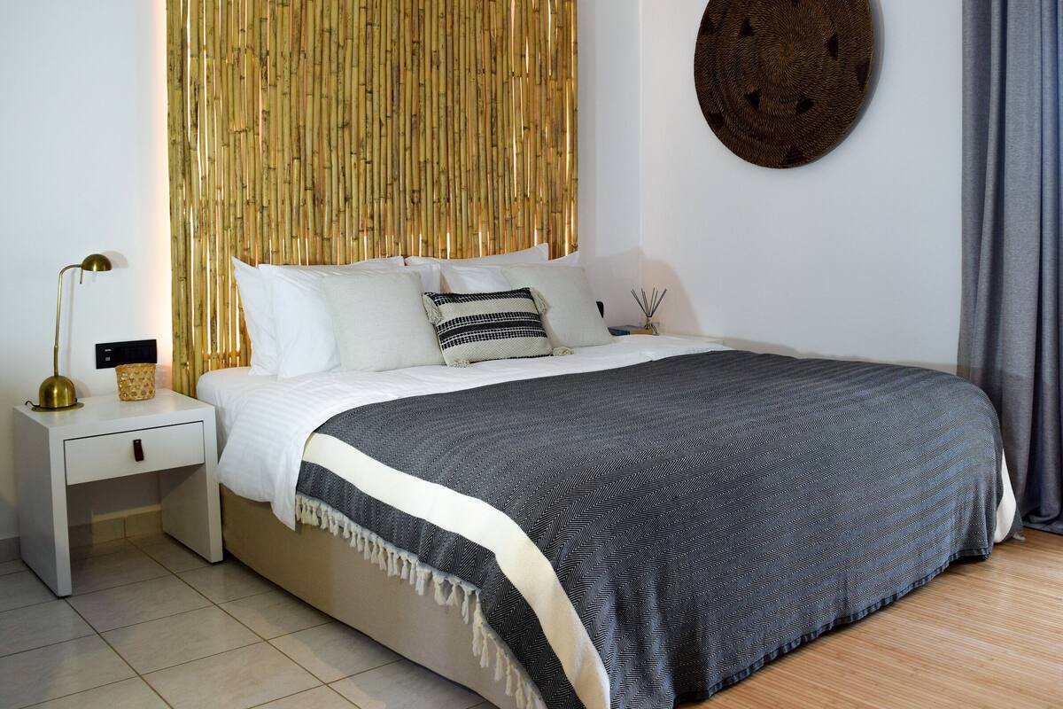 A modern bedroom with a bed, bedside tables, a wall-mounted round mirror, and a bamboo curtain.