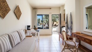 A modern living room with a sofa, coffee table, and dining area. There is a large window with a view of the outdoors. - Kanso Rooms (Chania)