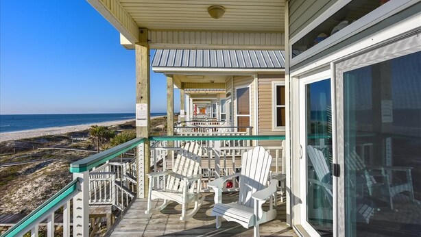 Een veranda aan het strand met Adirondack-stoelen, een glazen deur en uitzicht op de oceaan.