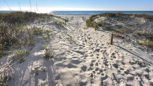 Een strandpad van zand met houten palen, dat naar de oceaan leidt.