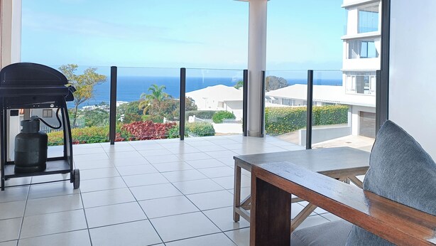 Un balcon avec vue sur l’océan, un barbecue et une table.