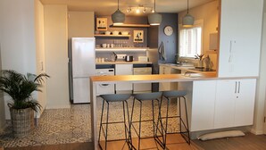 Une cuisine compacte dotée d’un îlot central, de tabourets de bar et d’un réfrigérateur.
