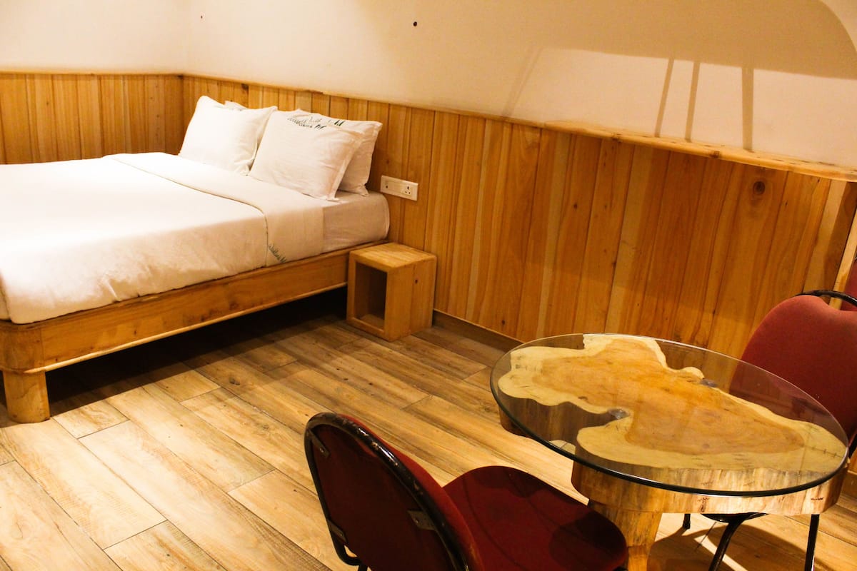 Une chambre avec un lit en bois, une petite table de chevet, une table en verre avec un plateau en bois et une chaise rouge.