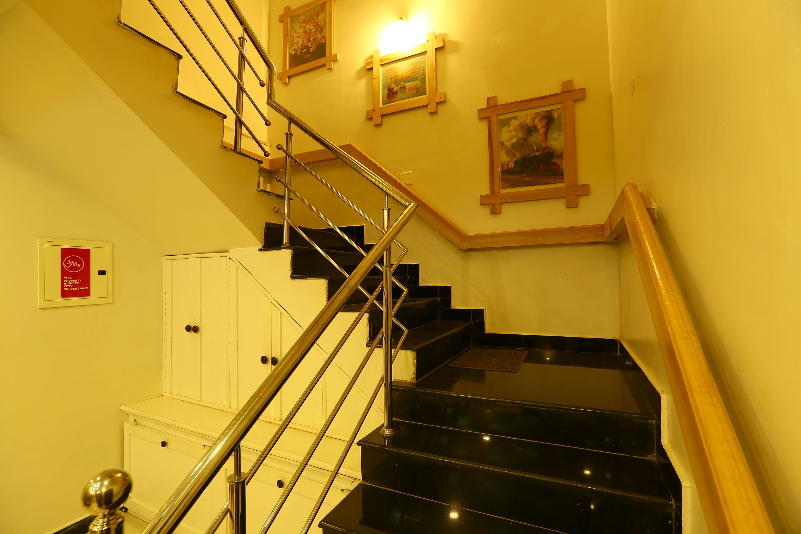 A staircase with black steps and a wooden handrail, leading to a landing with a white cabinet and a red sign.