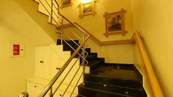A staircase with black steps and a wooden handrail, leading to a landing with a white cabinet and a red sign.