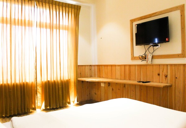 A hotel room with a bed, a mounted TV, wooden paneling, and a window with curtains.