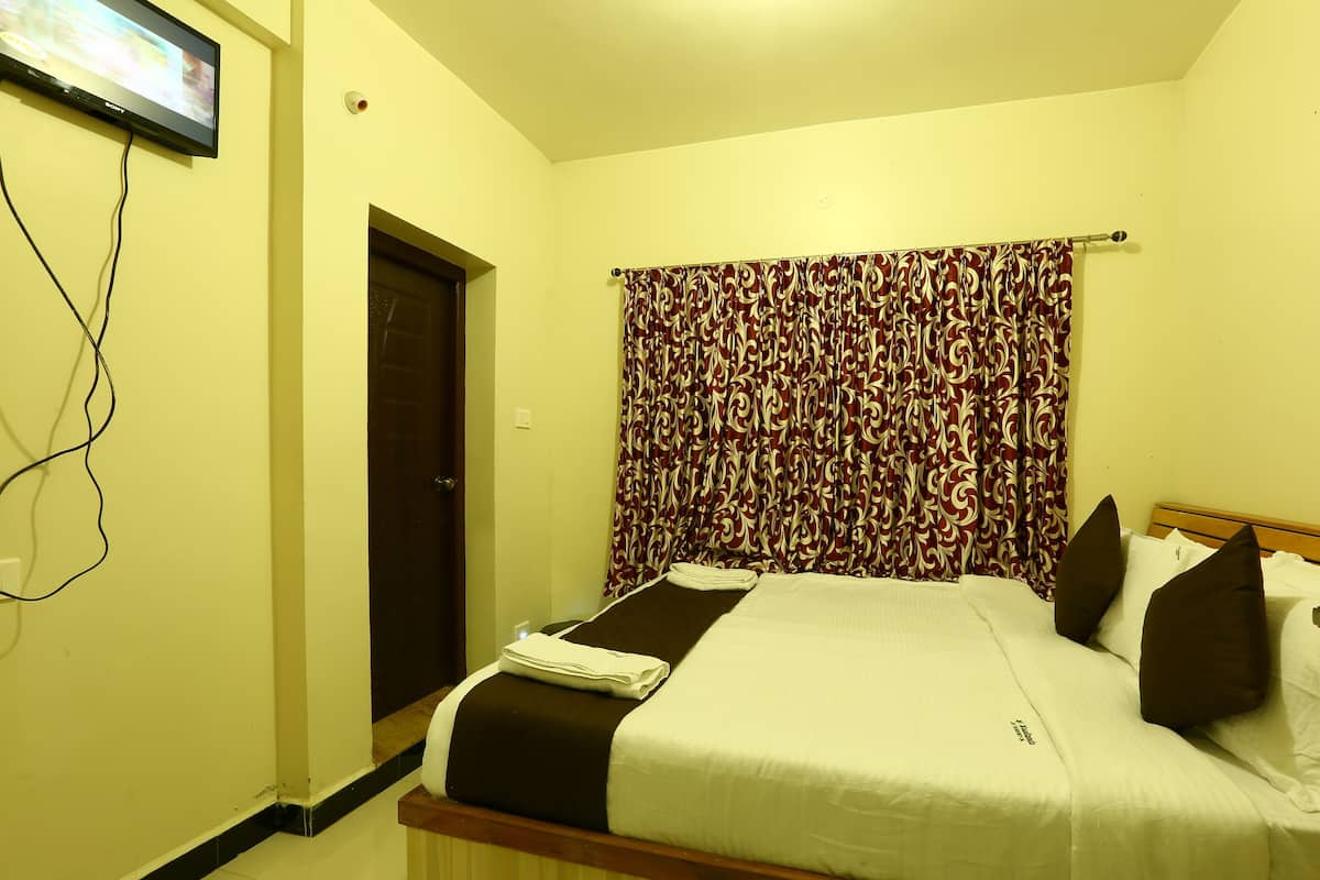 Une chambre d’hôtel avec un lit, des rideaux, un téléviseur fixé au mur et une porte.