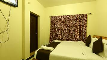 A hotel room with a bed, curtains, a television mounted on the wall, and a door.