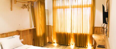 Quarto de hotel com cama, cabeceira de madeira, prateleira de madeira, televisão fixada na parede e janela com cortinas.
