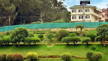 A residential building named "AL WOODLANDS RESIDENCY" with a well-maintained garden and a green netting structure.