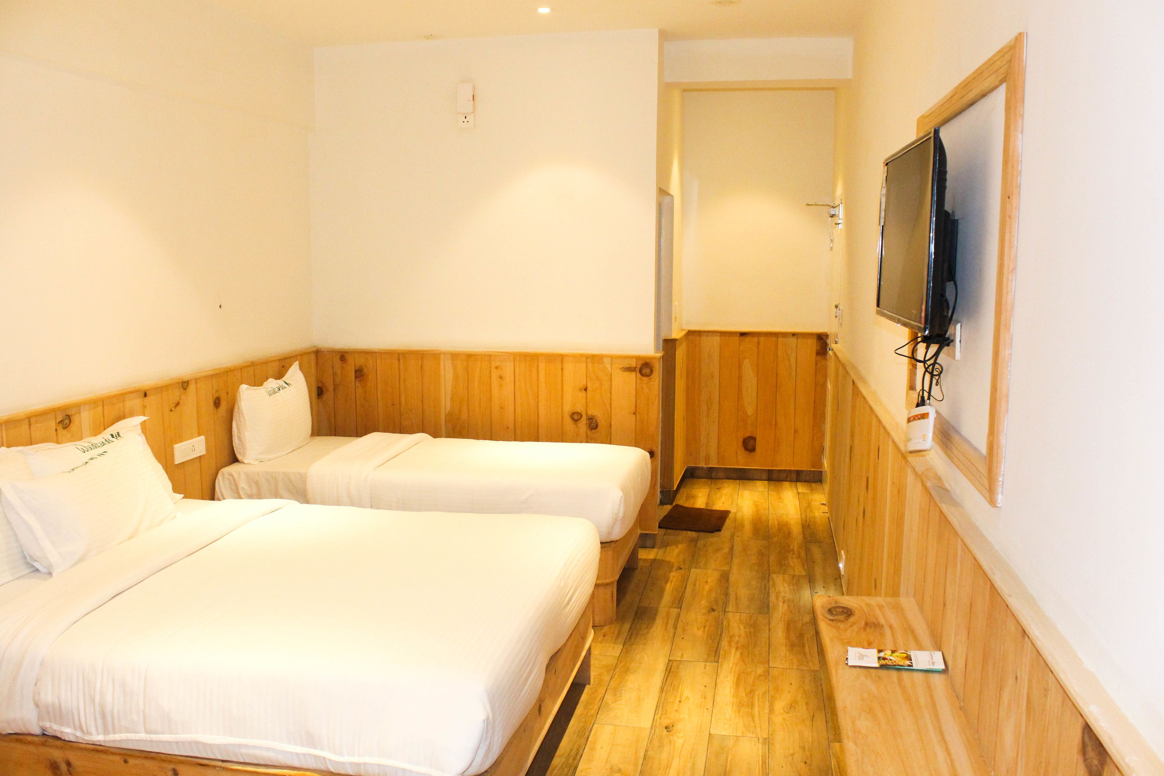 Une chambre d’hôtel avec deux lits simples, un lambris en bois, un téléviseur fixé au mur et un petit banc.