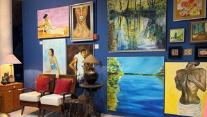 A room with a blue wall, a wooden chair, a table with a lamp, and various paintings. - La Vida Hostel (Samal)
