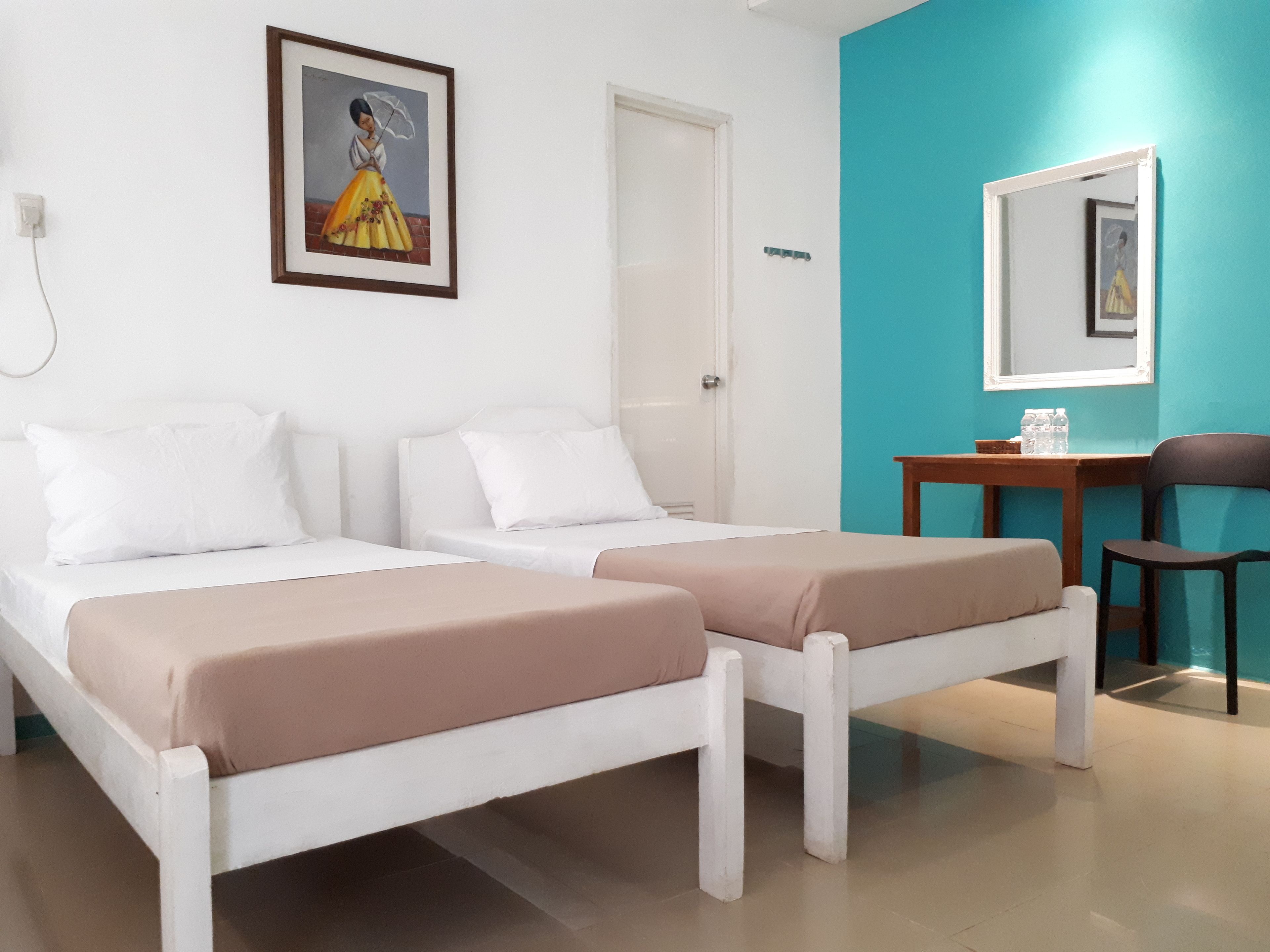 A room with two single beds, a desk with a chair, a mirror, and a framed picture on the wall.
