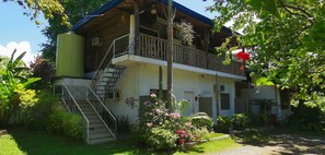 A two-story building with a balcony, a staircase, and a garden with flowers and plants. - La Vida Hostel (Samal)