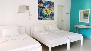 Una habitación con dos camas blancas, un cuadro abstracto de colores, un equipo de aire acondicionado blanco y una pequeña mesa con una cesta.