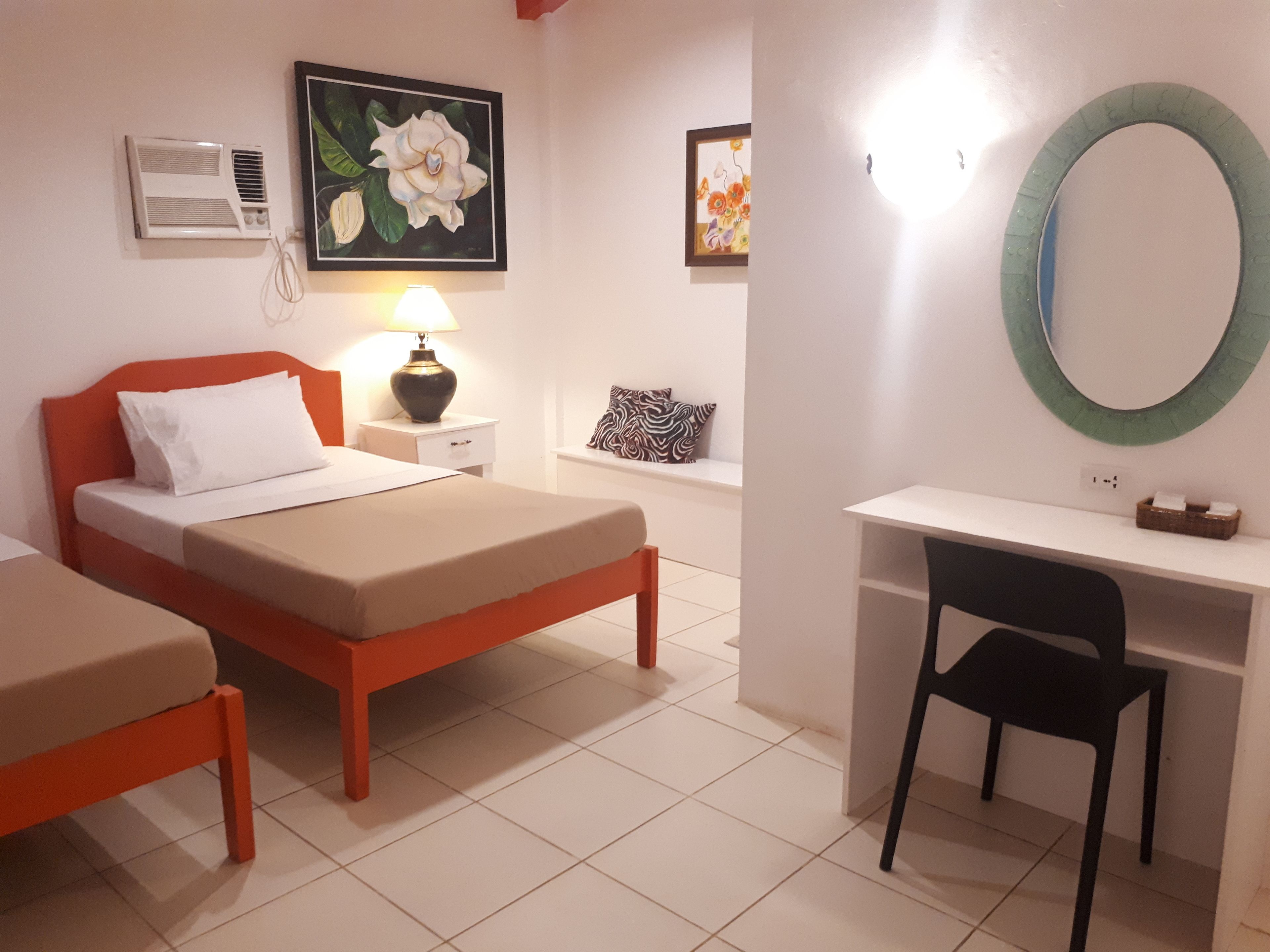 Un dormitorio con cama, mesita de noche, lámpara, escritorio, silla y espejo en la pared.