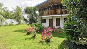 A two-story building with a balcony, surrounded by lush greenery and flowering plants. - La Vida Hostel (Samal)