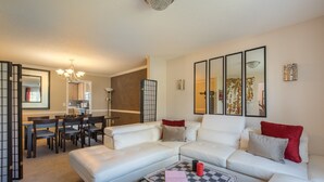A modern living room with a white sofa, a coffee table with a board game, and a dining area with wooden chairs and a table. - Comfort and Style on the Colonnade (Rex)
