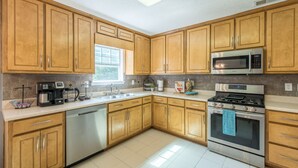 A kitchen with wooden cabinets, stainless steel appliances, and a window providing natural light. - Comfort and Style on the Colonnade (Rex)