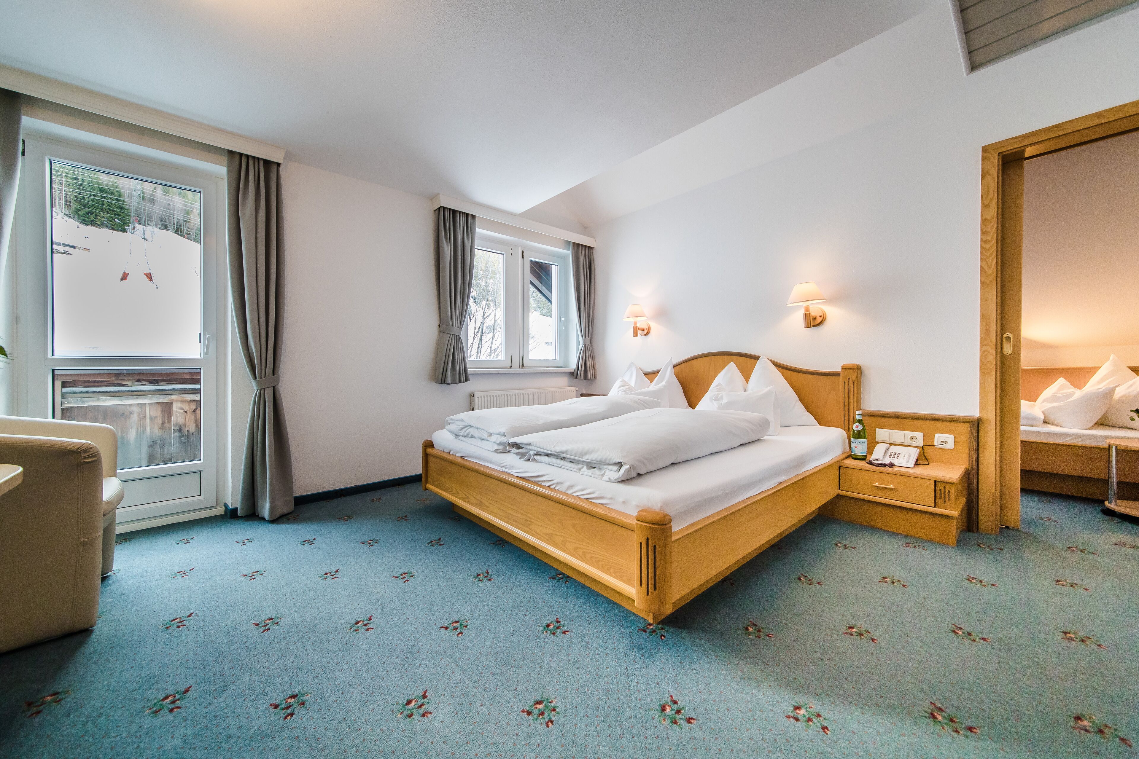 A hotel room with a bed, bedside tables, a chair, and a window with curtains.