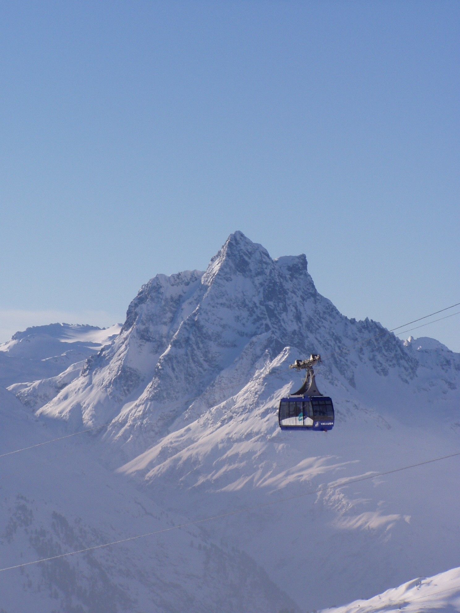 A cable car ascending a snow-covered mountain with a clear sky.