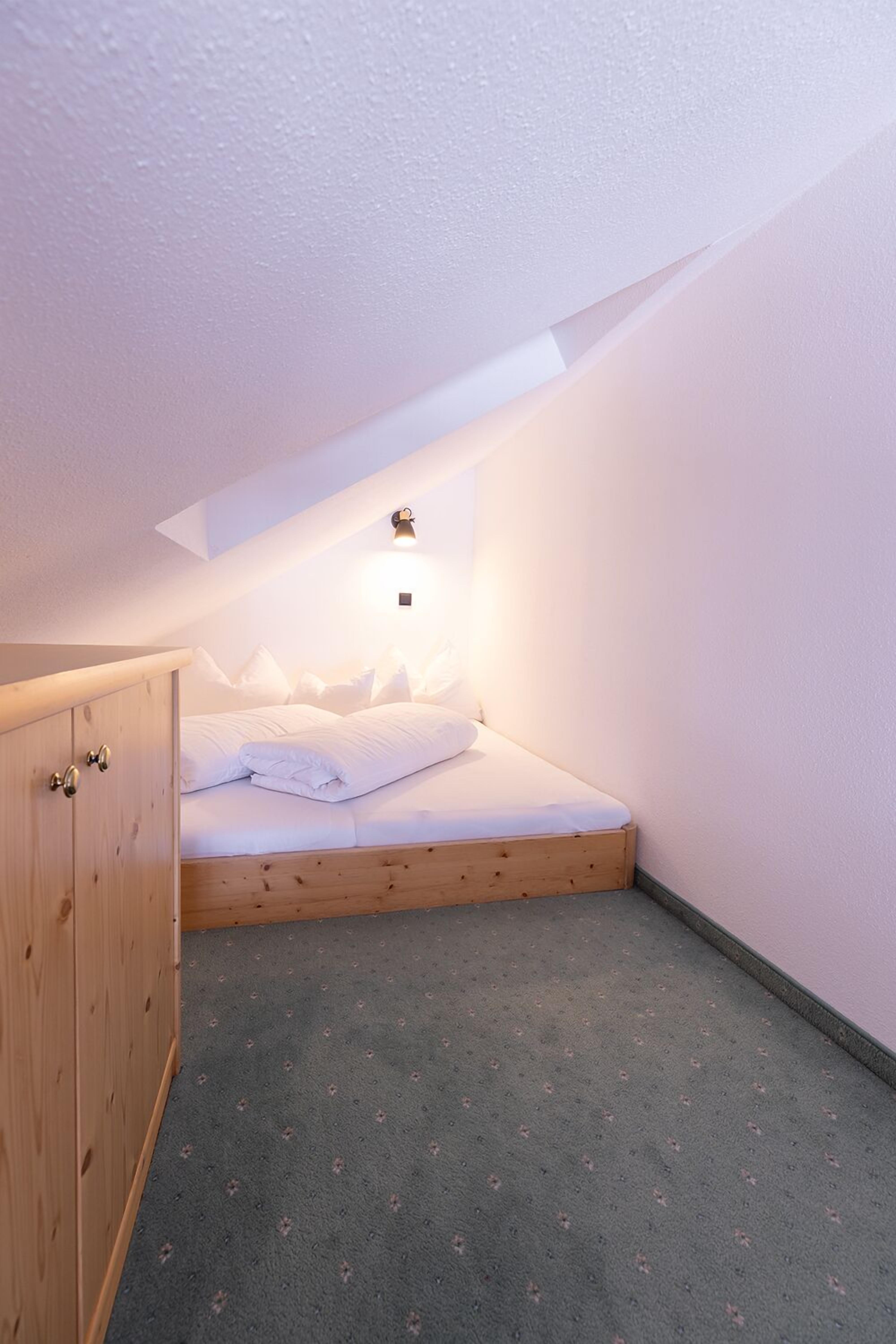 A small, cozy bedroom with a single bed, a wooden wardrobe, and a sloped ceiling.