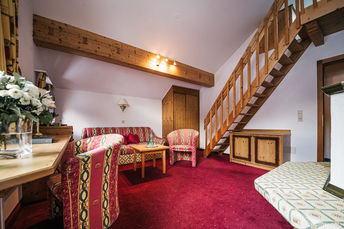 A cozy living room with a red carpet, wooden furniture, and a staircase.