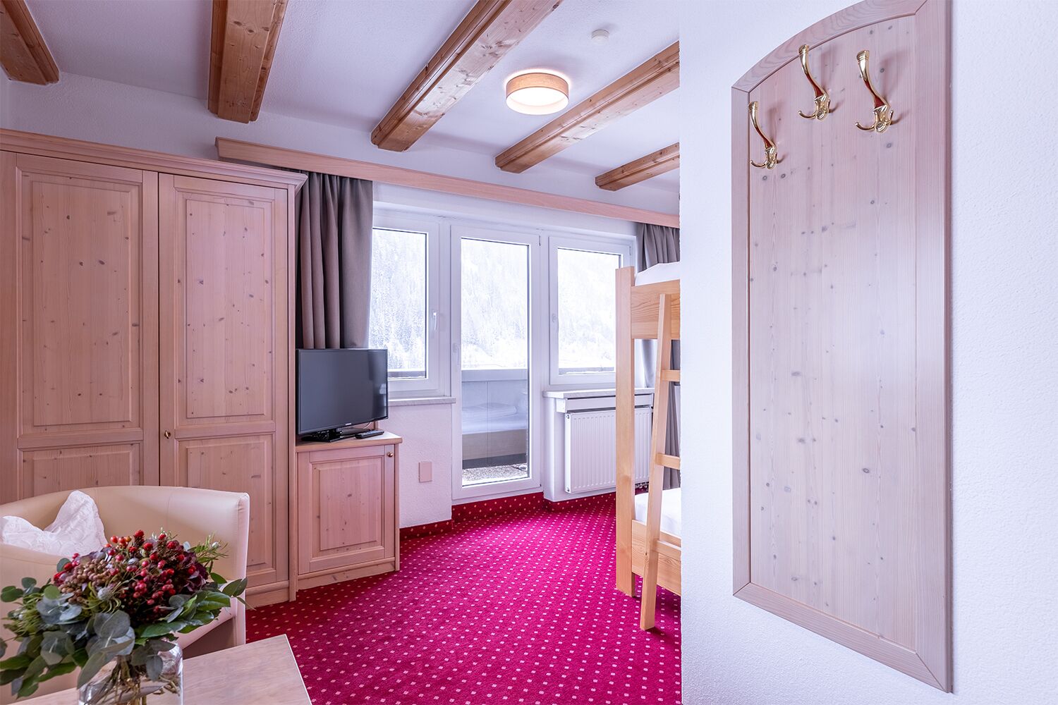 A room with wooden ceilings, a television on a cabinet, a red polka dot carpet, and a wooden door with hooks.