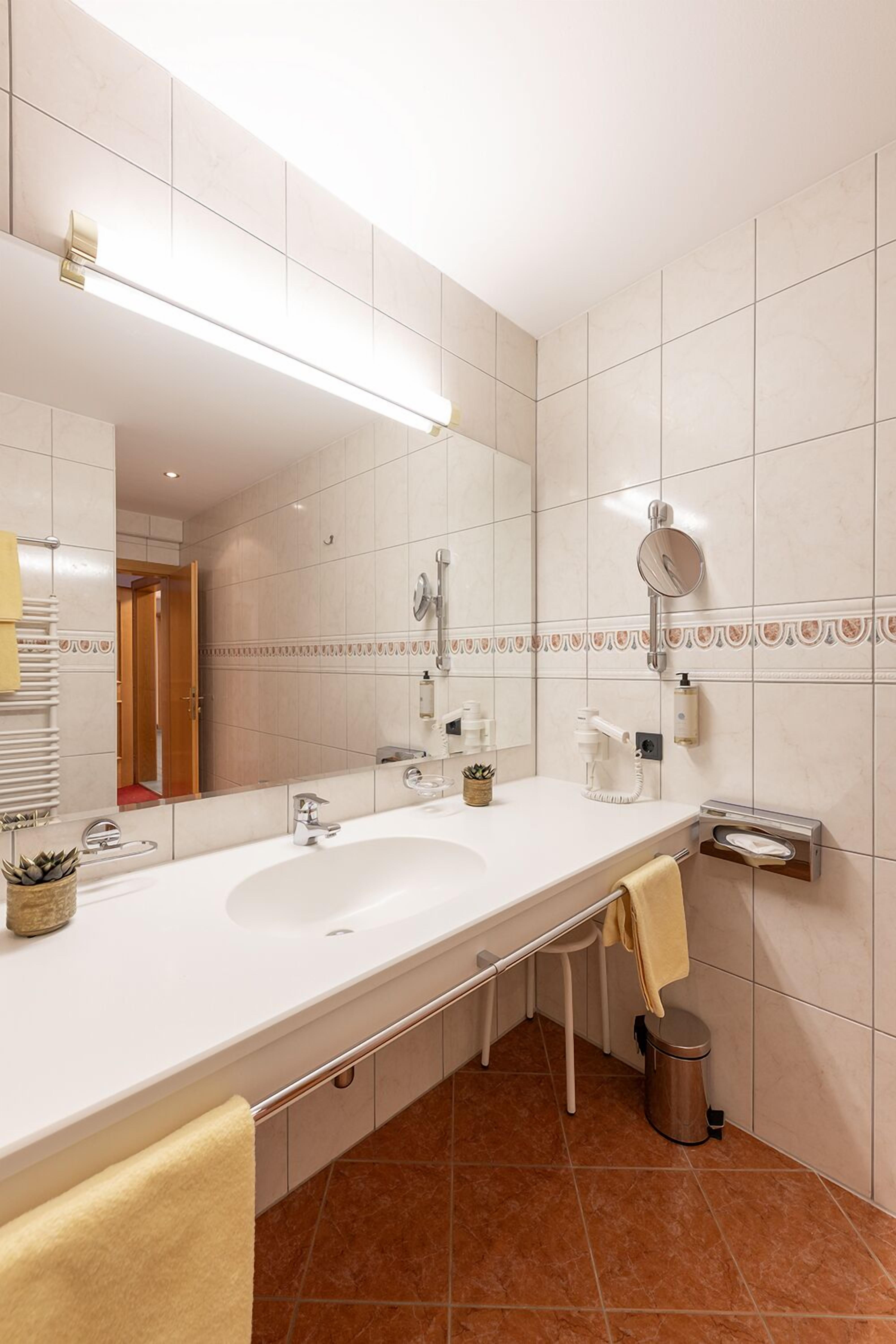 A modern bathroom with a large mirror, a white sink, a towel rack, and a trash bin.