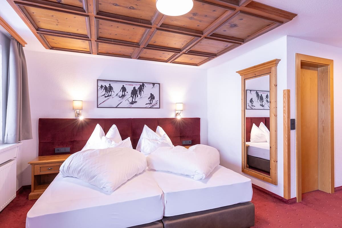 A hotel room with a wooden ceiling, a large bed with white bedding, two bedside tables, a mirror, and a framed picture on the wall.