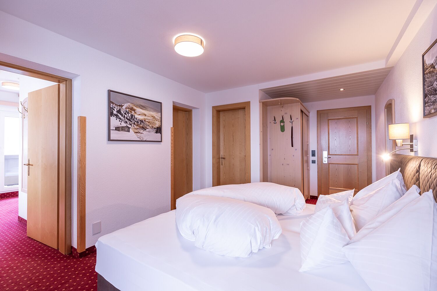 A hotel room with a large bed, two doors, a framed picture on the wall, and a red carpet.