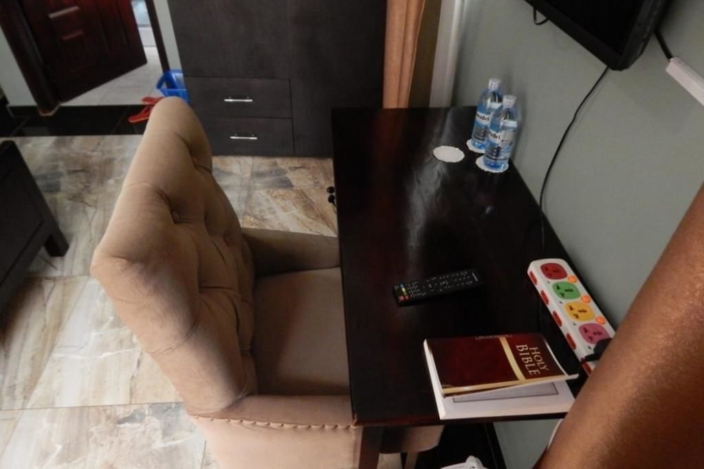 A room with a beige armchair, a dark wooden table with a remote control, a book, and two water bottles.